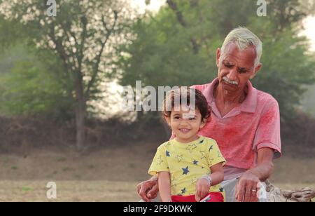 Primo piano di un nonno senior e di un piccolo nipote seduti insieme il campo Foto Stock