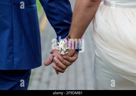 Un primo piano di sposi che tengono le mani con un minuscolo bouquet messo in un nastro sul polso della sposa Foto Stock