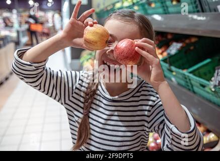 La bambina felice sceglie le mele in un negozio di alimentari. Shopping di alimentari divertente. Foto Stock