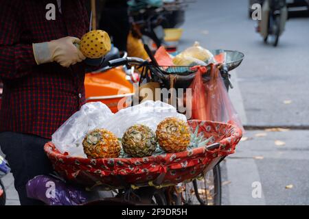 Una femmina che spellano un piccolo ananas in un tipico asiatico mercato all'aperto Foto Stock