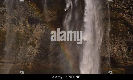 Vista in primo piano della famosa cascata Seljalandsfoss, una popolare destinazione turistica nel sud dell'Islanda vicino alla circonvallazione, sulla soleggiata giornata invernale arcobaleno. Foto Stock
