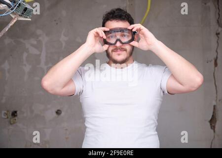 Giovane costruttore che indossa occhiali di sicurezza in un cantiere. Uomo che indossa occhiali di protezione. Foto Stock