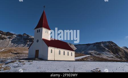 Bella vista della piccola chiesa del villaggio Vík í Mýrdal situato sulla costa meridionale dell'Islanda con pareti bianche e tetto di colore rosso. Foto Stock