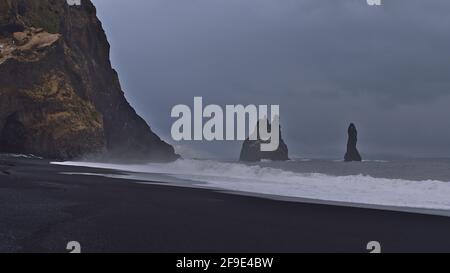 Vista della famosa spiaggia Reynisfjara, situata nel sud dell'Islanda, con sabbia nera e formazioni rocciose basaltiche durante il giorno invernale nuvoloso. Foto Stock