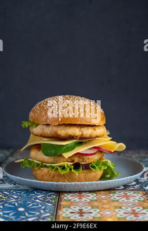 Panino hamburger, doppio filetto di pollo con formaggio, lattuga, rucola e rafano. Carne, verdure e pane. Ingredienti. Hamburger fatto in casa su un piatto Foto Stock
