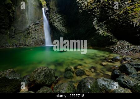 Cascate di Kozjak, Kobarid, Alpi Giulie, Slovenia in Europa. Superficie verde del lago nella gola rocciosa, grandi pietre bagnate in primo piano. Acqua nella grande wate Foto Stock