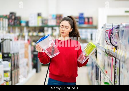 Una giovane donna caucasica sceglie tra due caraffe con un filtro dell'acqua in un negozio di elettrodomestici. Foto Stock