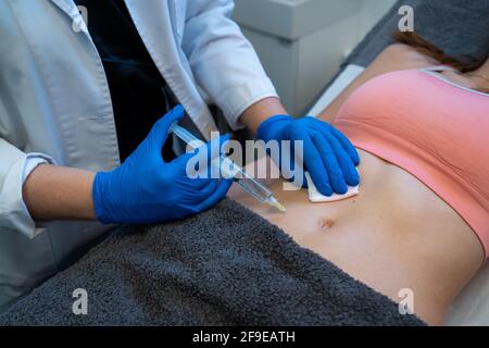 Dall'alto del raccolto anonimo estetista professionista che fa l'iniezione per la donna durante il trattamento della cellulite in clinica di bellezza Foto Stock