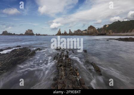 Vista panoramica delle formazioni rocciose sulla spiaggia di Gueirua vicino alla calma Mare sotto il cielo blu nelle Asturie Foto Stock