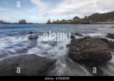 Vista panoramica delle formazioni rocciose sulla spiaggia di Gueirua vicino alla calma Mare sotto il cielo blu nelle Asturie Foto Stock