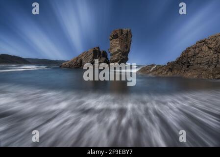 Maestosa vista delle formazioni rocciose sul bagnato Playon de Spiaggia di Bayas sotto il cielo nuvoloso nelle Asturie Foto Stock