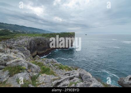 Vista mozzafiato della ruvida scogliera rocciosa vicino al mare calmo Ribadesella costa sotto il cielo grigio delle Asturie Foto Stock