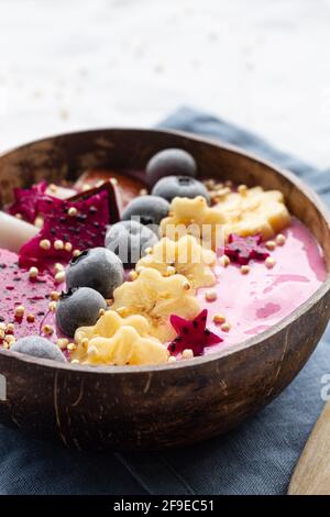 Dall'alto della ciotola potente piena di gustosi frullati vicino a colazione, banane mature e fette di frutta di drago con mirtilli Foto Stock