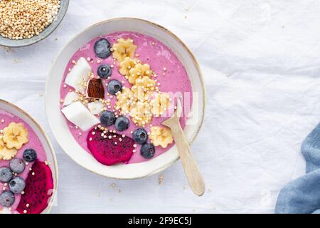 Dall'alto della ciotola potente piena di gustosi frullati vicino a colazione, banane mature e fette di frutta di drago con mirtilli Foto Stock