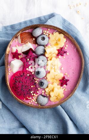 Dall'alto della ciotola potente piena di gustosi frullati vicino a colazione, banane mature e fette di frutta di drago con mirtilli Foto Stock
