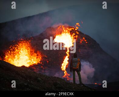 Uomo esploratore osservare il magma scintilla dal vulcano Fagradalfjall in Islanda tra le nuvole di fumo Foto Stock