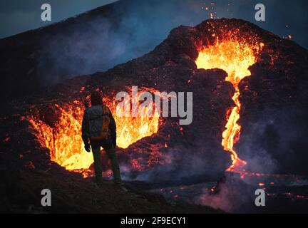 Uomo esploratore osservare il magma scintilla dal vulcano Fagradalfjall in Islanda tra le nuvole di fumo Foto Stock
