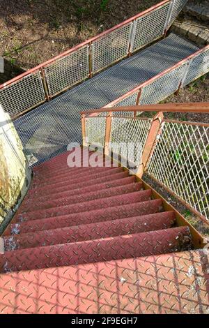 Vecchi gradini arrugginiti che conducono al piano inferiore ad un piccolo ponte Foto Stock