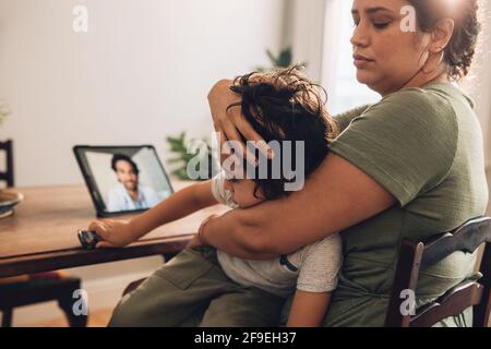 Donna con figlio malato che ha consultazione online con il medico di famiglia. Madre con il figlio che ottiene il consiglio in linea dal pediatra a casa. Foto Stock