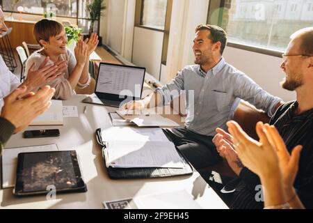I colleghi seduti intorno al tavolo e battono le mani per apprezzare il manager per il suo contributo di successo. uomini d'affari applaudono per giovani esecutivi Foto Stock