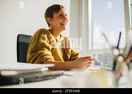 Donna felice executive seduto alla scrivania. Donna allegra seduto alla scrivania e guardando lontano in ufficio. Foto Stock