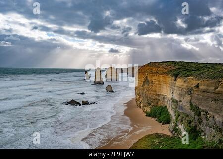 Il sole brilla attraverso le nuvole tempestose sulle formazioni rocciose dei dodici Apostoli sulla Great Ocean Road a Victoria, Australia Foto Stock