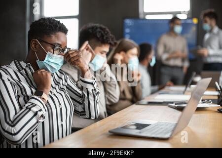 Persone internazionali che indossano maschere mediche utilizzando un computer portatile Foto Stock