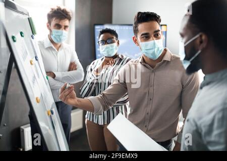 Dipendente in maschera medica protettiva che presenta la strategia aziendale sulla lavagna Foto Stock