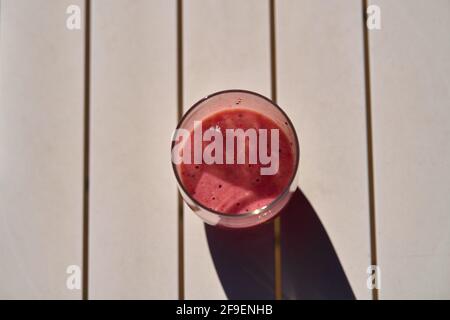 Frullato di frutta di colore rosso su tavola bianca sotto la luce del sole Foto Stock