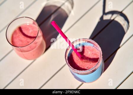 Due frullati di frutta di colore rosso sul tavolo bianco sotto luce solare Foto Stock