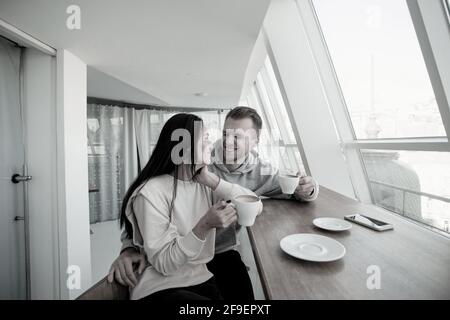 Giovane coppia che flirta nel bar. Bella donna con lunghi capelli scuri e uomo bello con elegante capelli guardare l'un l'altro, tenere il caffè Foto Stock