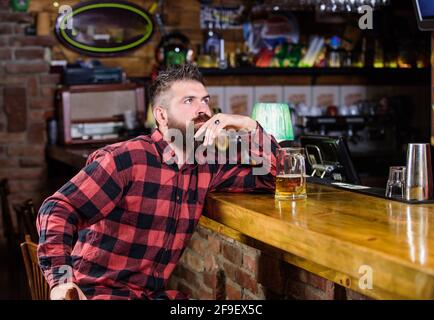 Ordinare bevande alcoliche. Il bar è un luogo rilassante dove sorseggiare un drink e rilassarsi. Uomo con barba trascorri il tempo libero al bar scuro. L'uomo brutale, portatore di hipster, si siede al bar Foto Stock