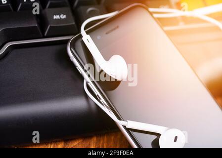 Smartphone e cuffie sulla tastiera di un computer portatile. Clubhouse è un'applicazione di chat audio. Foto Stock
