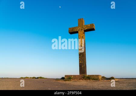 Grande vecchia croce di pietra cristiana coperta di lichene giallo luminoso di fronte ad un cielo blu chiaro all'inizio del tramonto. Concetto di fede e religione. Foto Stock