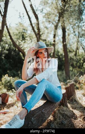 Un'immagine verticale di un'elegante donna caucasica seduta sopra un ceppo di albero in una foresta Foto Stock