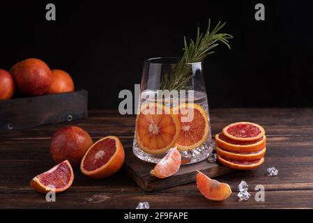 Bicchiere con acqua funzionale con fette di arancia e rosmarino su sfondo di legno scuro, succo d'arancia, primo piano. Foto Stock