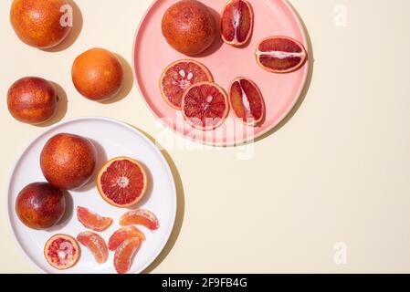 Piastre con arance di sangue intere e tagliate a fette su sfondo giallo in luce intensa, vista dall'alto, primo piano. Foto Stock