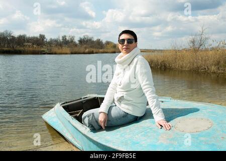 Una donna di mezza età gode dell'aria fresca all'inizio della primavera sul fiume. La donna indossa un pullover sportivo bianco. Foto Stock