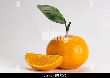 Vista laterale di mandarino o Citrus reticulata un intero e un pezzo con foglia su sfondo bianco con tracciato di ritaglio. Foto Stock