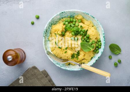 Purè di patate con burro, piselli verdi, cipolle, basilico in una ciotola bianca su un fondo di ardesia, pietra o calcestruzzo leggero. Vista dall'alto con primo piano. Foto Stock