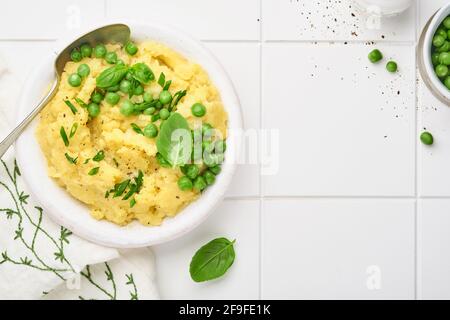 Purè di patate con burro, piselli verdi, cipolle, basilico su sfondo bianco in ceramica. Vista dall'alto con primo piano. Foto Stock