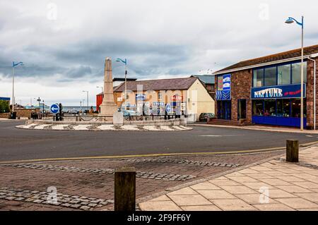 L'edificio classificato di grado 11, Seahouses War Memorial, è situato al centro di una grande isola trafficata delimitata da un lato da negozi e da una caffetteria Foto Stock