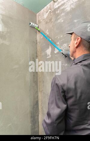 Un uomo costruttore che innescarono un muro prima di fare ulteriori lavori con un rullo da costruzione Foto Stock