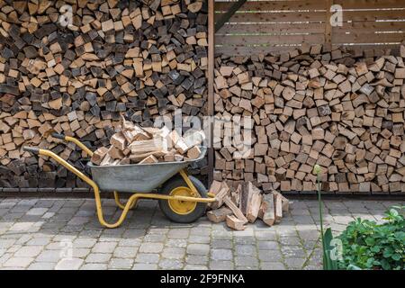 Pila impilata di legna da ardere e un carriola con pezzi di legna di fuoco da immagazzinato Foto Stock