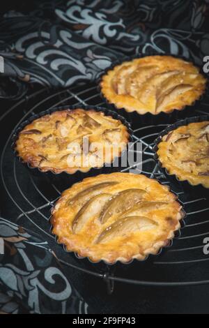 Tartine di mela cotte al forno in piatti di crostata nera su una griglia di raffreddamento con un panno modellato. Primo piano verticale. Foto Stock