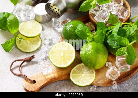 Rinfrescante cocktail estivo freddo Mojito. Ingredienti di menta, lime, ghiaccio e utensili da bar su un tavolo in pietra o cemento. Foto Stock