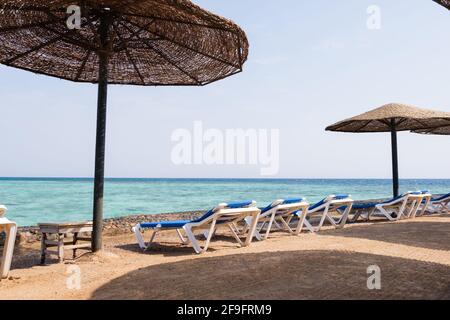 Lettini e ombrelloni in paglia lungo la spiaggia sdraio blu Con Vista Mare Foto Stock