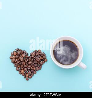 Tazza di caffè nero caldo e chicchi di caffè a forma di cuore su sfondo blu, spazio di copia, vista dall'alto, forma quadrata. Caffè del mattino Foto Stock