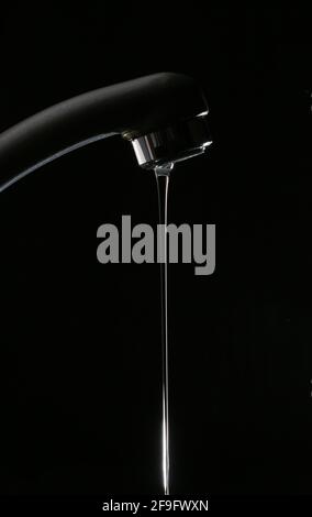 Acqua che scorre da un nuovo rubinetto su sfondo nero in cucina con una grande casa Foto Stock