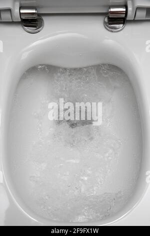 Un nuovo wc bianco durante l'imbragatura d'acqua su uno sfondo di piastrelle grigie sulla parete Foto Stock